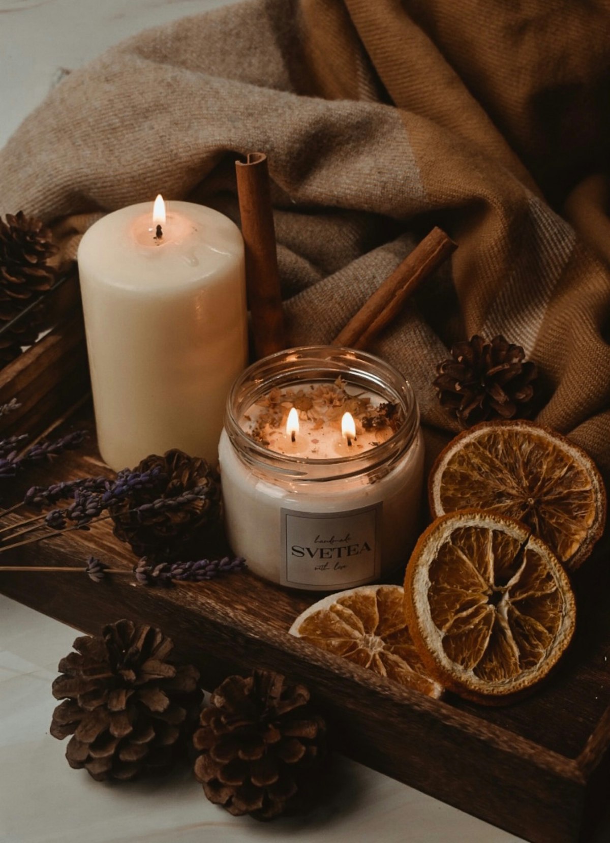 Lit candles on a wooden tray with pinecones and dried orange